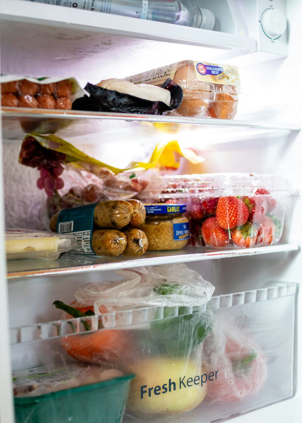 A real, lived-in fridge: eggs, strawberries, sausages, fresh produce — plenty of food, no obvious dinner